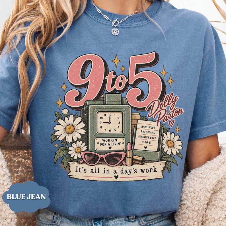 May include: A blue t-shirt featuring a graphic print with the text 9 to 5, Dolly Parton, and It's all in a day's work. The design includes a vintage clock, daisies, pink cat-eye glasses, a lipstick tube, and a sign listing hard work.