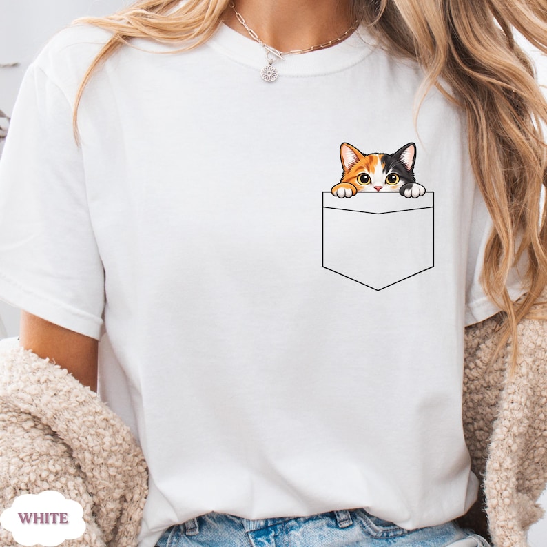 A person wearing a white t-shirt with a cat graphic peeking out of a pocket.