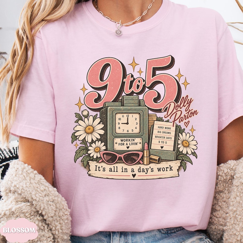May include: A light pink t-shirt featuring a graphic with the text 9 to 5, Dolly Parton, and It's all in a day's work. The design includes a vintage clock, pink sunglasses, a lipstick tube, a notepad, and white daisy flowers with green leaves.
