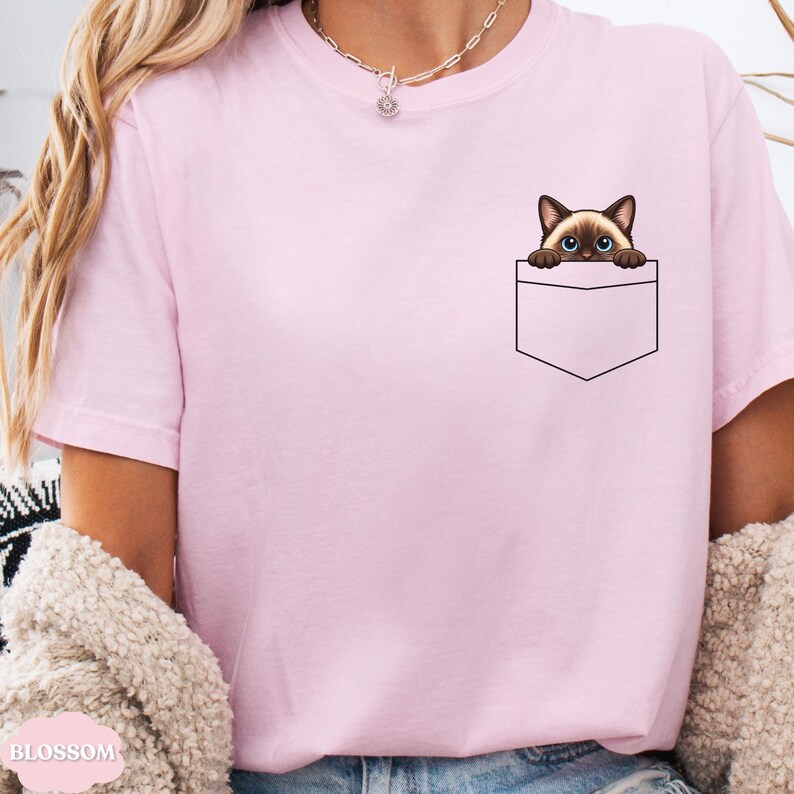 A person wearing a pink t-shirt with a cat design peeking out of a pocket.
