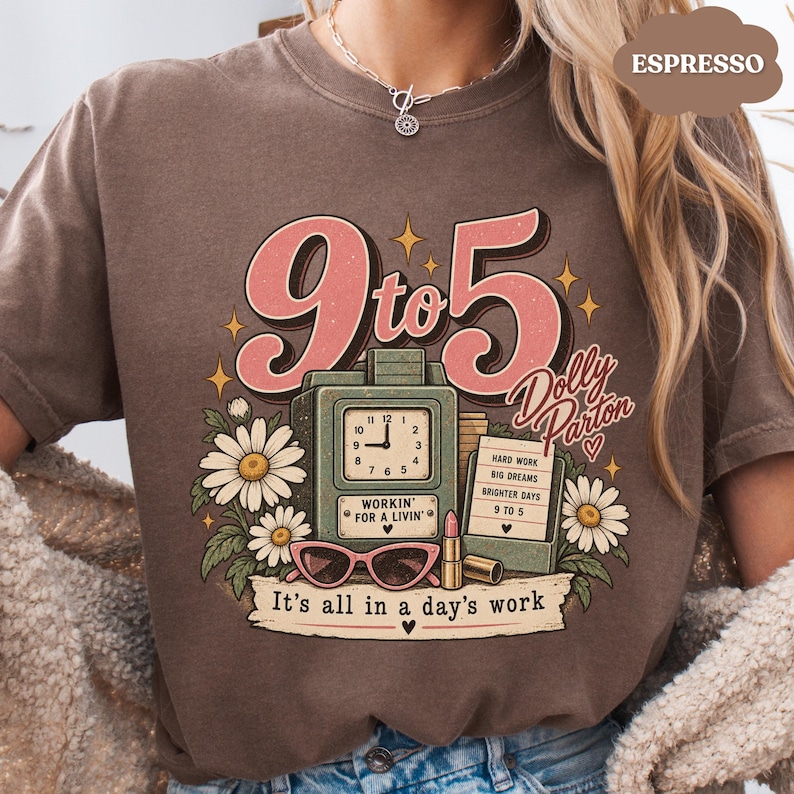 May include: A brown t-shirt featuring a graphic print with the text 9 to 5, Dolly Parton, Workin' for a Livin', and It's all in a day's work. The design includes a vintage clock, daisies, pink cat-eye glasses, a lipstick, and a small sign.