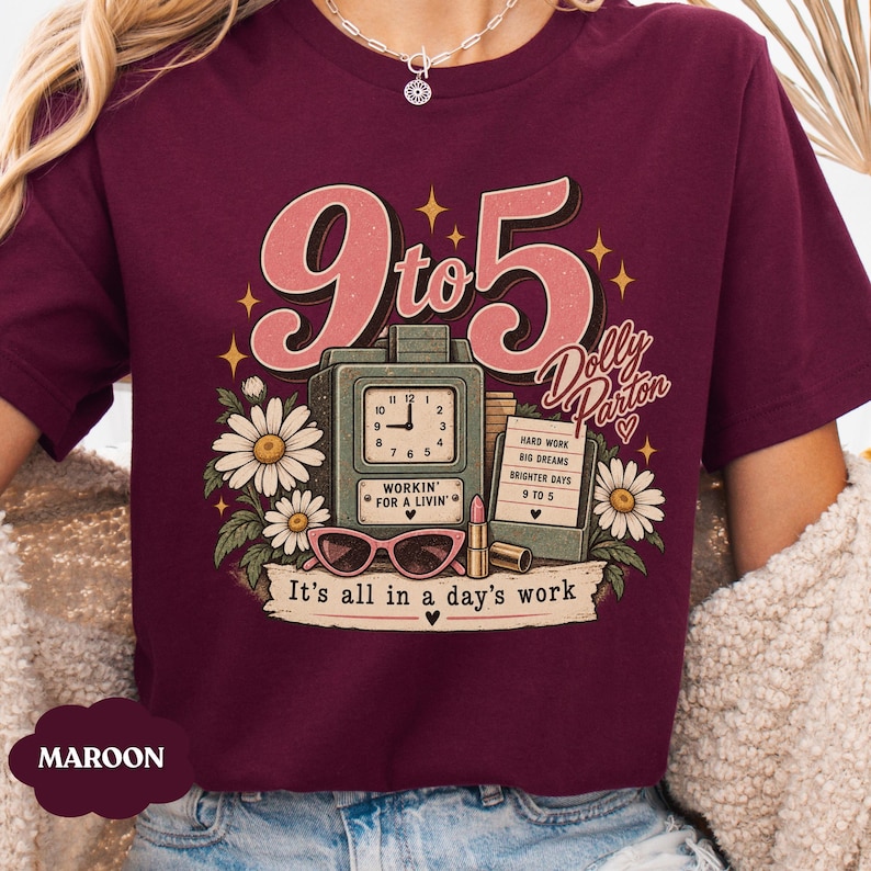May include: A maroon t-shirt featuring a graphic print with the text 9 to 5, Dolly Parton, and It's all in a day's work. The design includes a vintage clock, a sign with text, pink cat-eye glasses, a lipstick tube, and white daisy flowers.