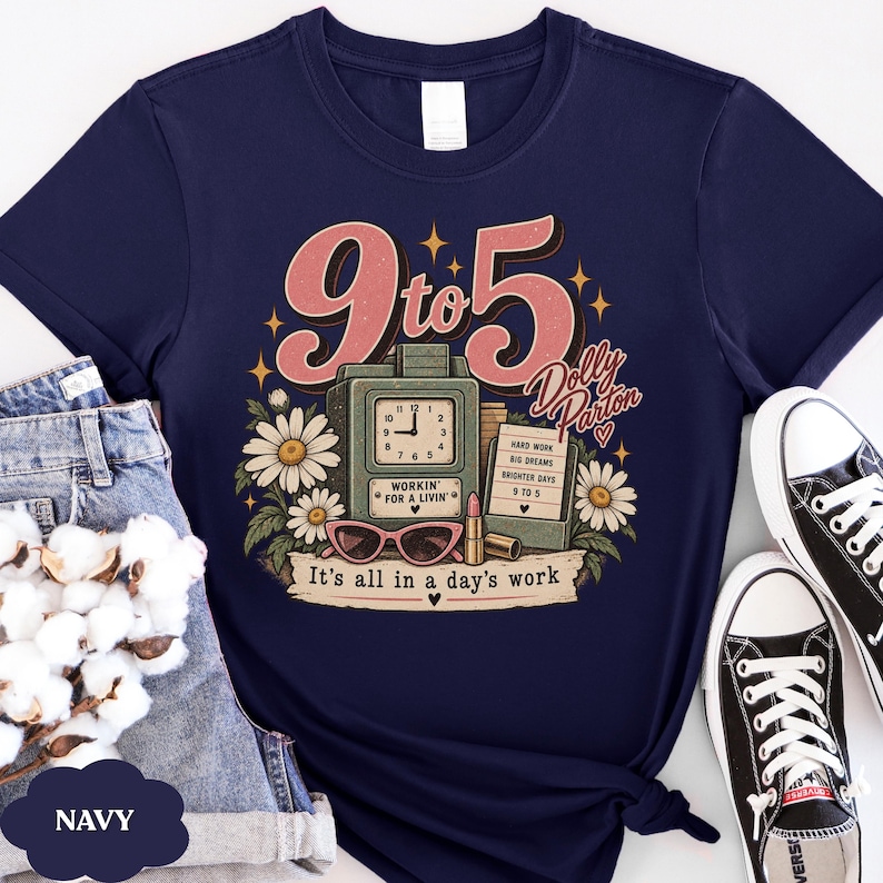 May include: A navy blue t-shirt featuring a graphic print with the text 9 to 5, Dolly Parton, and It's all in a day's work. The design includes a vintage clock, a lipstick, sunglasses, daisies, and a sign listing Hard Work, Big Dreams, Brighter Days.