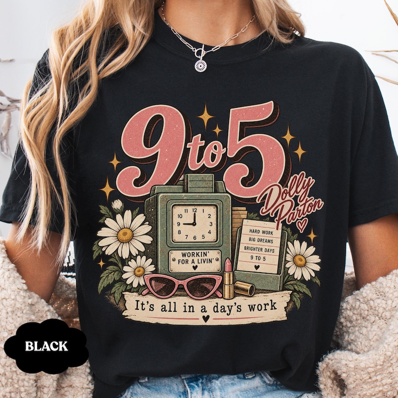 May include: A black t-shirt featuring a graphic print with the text 9 to 5, Dolly Parton, and It's all in a day's work. The design includes a green time clock, white daisies, pink cat-eye sunglasses, a lipstick tube, and a notepad with text.