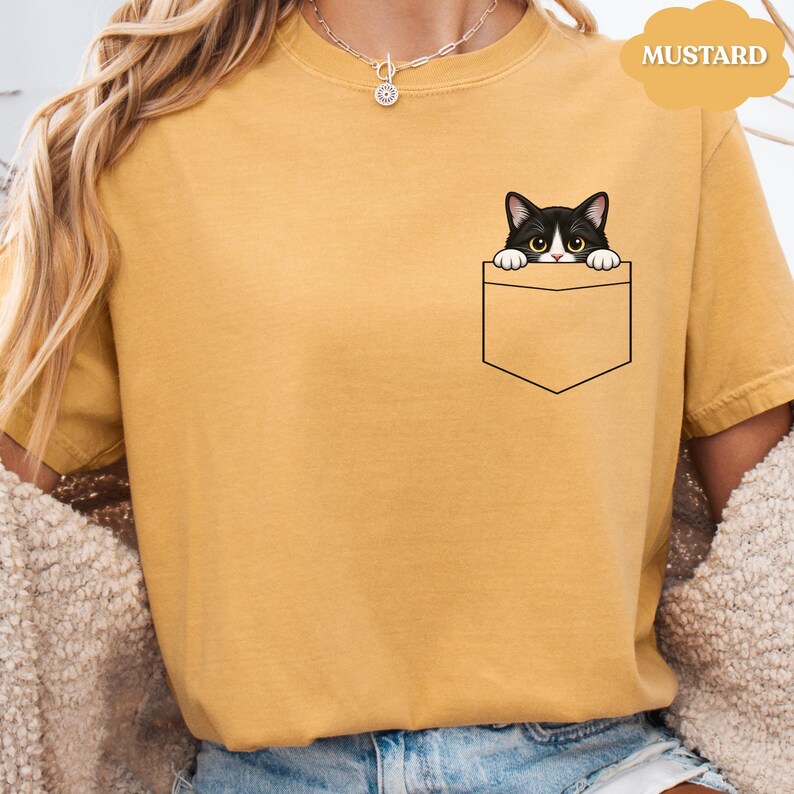 A person wearing a yellow t-shirt with a black and white cat graphic peeking out of a pocket.