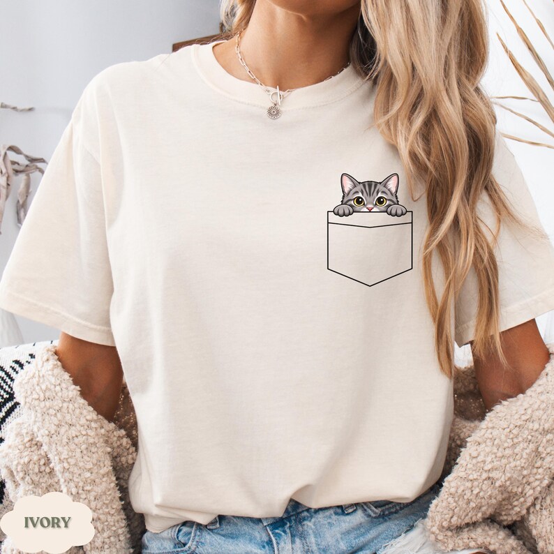 A woman wearing a white t-shirt with a cat graphic peeking out of a pocket.