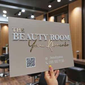 Puede incluir: Un letrero rectangular con el texto "THE BEAUTY ROOM" en letras blancas y doradas. El nombre "Yana Khomenko" está escrito en escritura dorada. También hay un código QR e información de contacto.