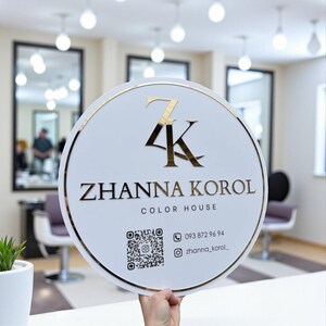 Puede incluir: Un letrero redondo blanco con borde y letras doradas. El letrero dice "Zhanna Korol Color House" con un logotipo "ZK" dorado. Incluye un código QR, número de teléfono y nombre de usuario de Instagram.