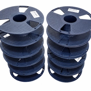 Puede incluir: Dos pilas verticales de cinco bobinas de filamento para impresora 3D de plástico azul oscuro cada una. Las bobinas circulares presentan un diseño perforado con un núcleo central y varias aberturas rectangulares en el borde exterior, con etiquetas blancas.