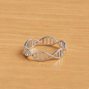 May include: A silver-toned ring featuring a continuous, open-work design that mimics the double helix structure of a DNA strand. The band is constructed from two intertwined metal ribbons connected by small, evenly spaced vertical bars.