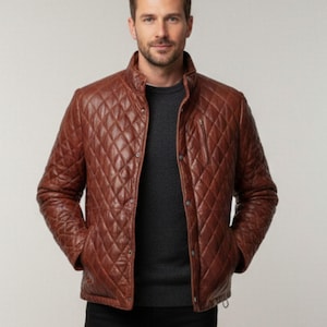 Puede incluir: Chaqueta de cuero acolchada marrón con cuello alzado y bolsillo delantero con cremallera. La chaqueta tiene un patrón de diamantes y cierres de botón. El modelo lleva un jersey gris oscuro debajo.