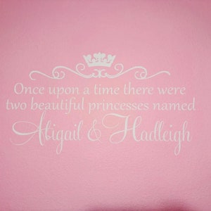 Puede incluir: Pared rosa con una calcoman&iacute;a de vinilo blanco que dice "&Eacute;rase una vez dos hermosas princesas llamadas Abigail & Hadleigh". La calcoman&iacute;a presenta una corona y un adorno decorativo.