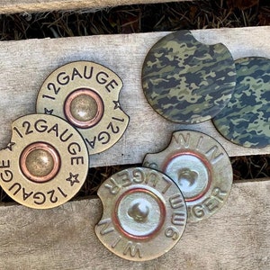 May include: Four round, brown and gold, 12 gauge shotgun shell coasters with a camouflage pattern coaster and a black and green camouflage pattern coaster.