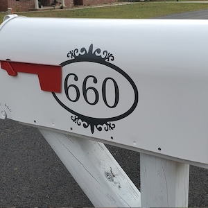 May include: White mailbox with a black oval sticker with the number 660 in the center. The sticker has a decorative black border.