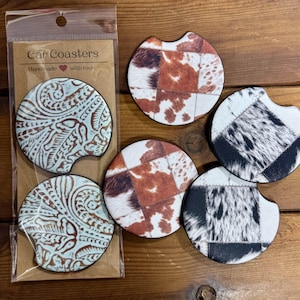 May include: Car coasters with a variety of designs. Some are patterned with cowhide patches in brown, white, and black. Others have a turquoise and brown embossed floral design. The packaging reads "Car Coasters Handmade with love."