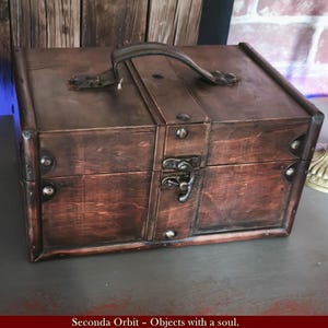 Op de afbeelding: Een donkerbruine houten kist met een metalen handvat en sluiting. De kist heeft metalen accenten en is rechthoekig van vorm. De tekst "Objects with a soul" staat onderaan de afbeelding.