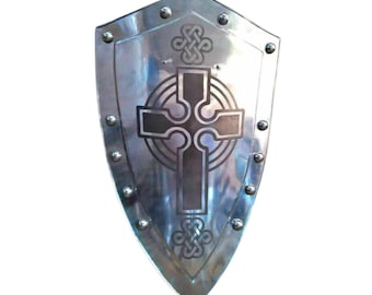 May include: A silver-colored shield with a pointed bottom and a Celtic cross design in the center. The shield has a series of rivets around the edge and decorative knotwork above and below the cross.