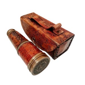 Puede incluir: Un telescopio de estilo vintage con estuche de cuero. El telescopio es marrón con detalles en latón, y el estuche está grabado con motivos florales. El telescopio tiene el texto "DOLLOND LONDON 1920" en la base.
