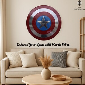 May include: A large, round shield with a red, silver, and blue design, featuring a silver star in the center. The shield is mounted on a beige wall above a beige sofa with decorative pillows. Text reads: Enhance Your Space with Heroic Vibes.