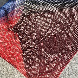 Könnte beinhalten: Ein handgefertigter, offen gewebter Schal mit Farbverlauf. Der Schal wechselt von Blau zu Rot, mit einem zentralen Abschnitt in tiefem Burgunderrot. Das komplizierte Muster erzeugt einen strukturierten, spitzenartigen Effekt, zum Tragen oder Dekorieren.