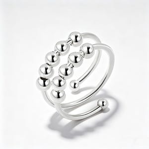 May include: A silver ring with a spiral design. The ring has two bands, one with a series of small, round beads and the other a smooth, curved band. The beads are evenly spaced, adding texture to the jewellery.