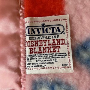 May include: A close-up of a Disneyland blanket with a tag that reads "Invicta" and "100% Acrylic Pile". The blanket is pink, red, and blue. The tag also says "Made in Australia".
