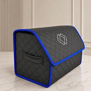 Op de afbeelding: Zwarte gewatteerde opbergcontainer met blauwe rand en een geometrisch ontwerp op het deksel. De container heeft een handvat en staat op een marmeren oppervlak. Ontworpen voor opslag.