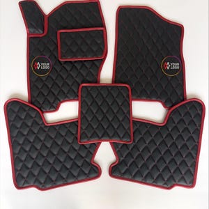 May include: Set of black car floor mats with red trim and diamond stitching. The mats have a quilted pattern and a logo in a circle. The set includes mats for the driver and passenger sides, as well as smaller mats.