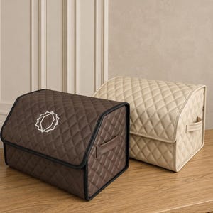 Op de afbeelding: Twee gewatteerde opbergdozen. E&eacute;n is bruin met een wit geometrisch ontwerp en zwarte rand. De andere is beige. Beide hebben handvatten en diamantstiksels. Ze staan op een houten oppervlak.
