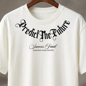 Puede incluir: Camiseta blanca de cuello redondo con la frase "Predict The Future" en fuente gótica en el pecho. Debajo, en fuente cursiva, se lee "Success Final" con "Continue That Counts" debajo.