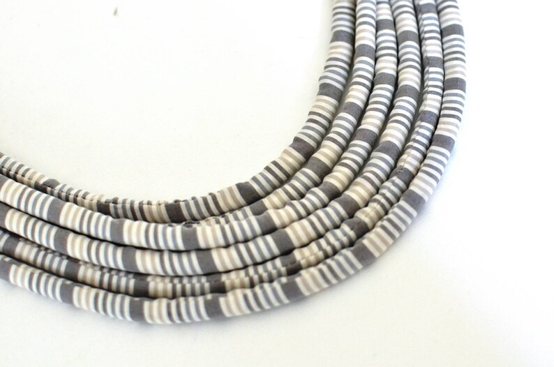 May include: A gray and white striped fabric necklace. The necklace is made of multiple strands of fabric that are woven together.