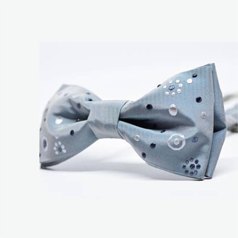 Peut inclure: Un n&oelig;ud papillon bleu clair avec un motif de pois blancs et argent&eacute;s.