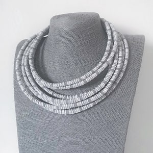 May include: A multi-strand necklace made of gray and white beads. The necklace is layered and has a chunky, bold look.