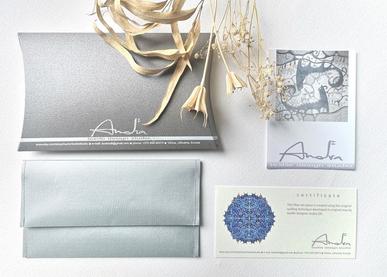 May include: A certificate of authenticity for a fiber art piece. The certificate is printed on a light beige card with a blue and white mandala design in the upper left corner. The text reads "This fiber art piece is created using the original textile technique developed in original way by textile designer Audra ZB." The certificate is signed "Audra textile design studio" with a website address and phone number.