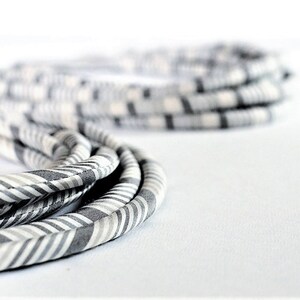May include: A close-up of a gray and white striped fabric cord. The cord is coiled and twisted, creating a textured and layered effect.