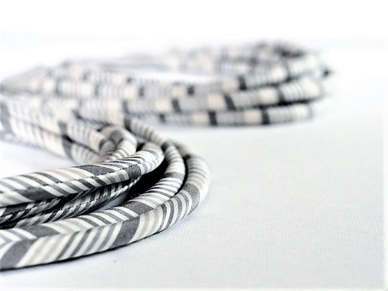 May include: A close-up of a gray and white striped fabric cord. The cord is coiled and twisted, creating a textured and layered effect.