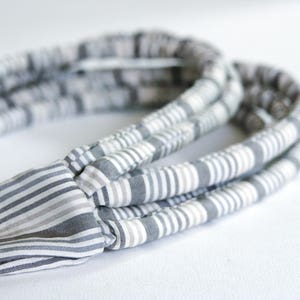 May include: A gray and white striped headband made of fabric. The headband is folded in on itself, creating a thick, layered look.