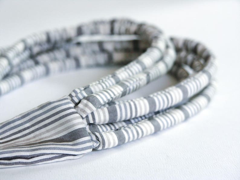 May include: A gray and white striped headband made of fabric. The headband is folded in on itself, creating a thick, layered look.