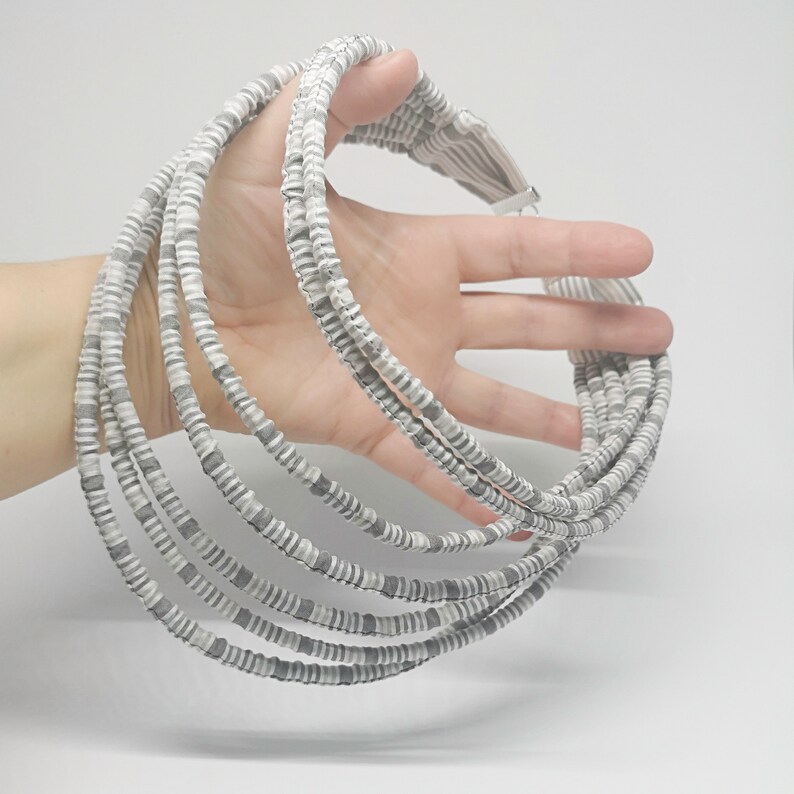 May include: A multi-strand necklace made of gray and white beads. The necklace is made of several layers of beads, creating a thick and chunky look.