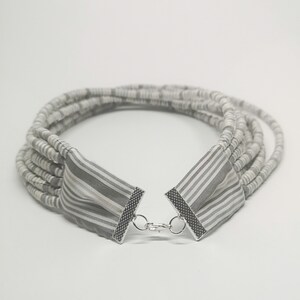 May include: A multi-strand necklace made of gray and white fabric with a silver clasp.