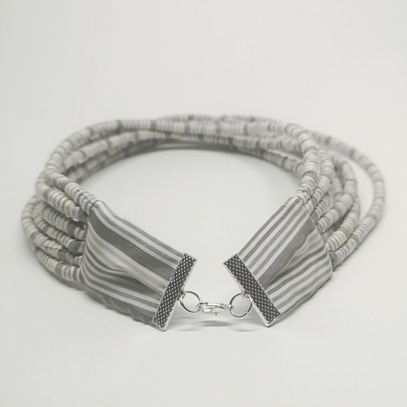 May include: A multi-strand necklace made of gray and white fabric with a silver clasp.