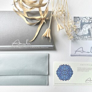 Peut inclure: Un certificat d'authenticit&eacute; pour une &oelig;uvre d'art textile. Le certificat est imprim&eacute; sur du papier cartonn&eacute; blanc avec un motif de mandala bleu et blanc dans le coin sup&eacute;rieur gauche. Le texte indique "Certificat" et "Cette &oelig;uvre d'art textile est cr&eacute;&eacute;e en utilisant la technique textile originale d&eacute;velopp&eacute;e de mani&egrave;re originale par la cr&eacute;atrice textile Anda Zb." Le certificat est sign&eacute; "Anda" et comprend le nom de l'entreprise "Anda textile design studio" et les coordonn&eacute;es.