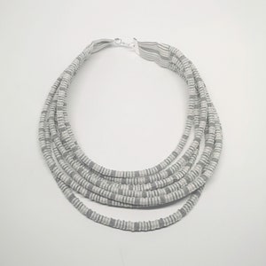 May include: A multi-strand necklace made of gray and white striped fabric. The necklace is layered and has a simple silver clasp.