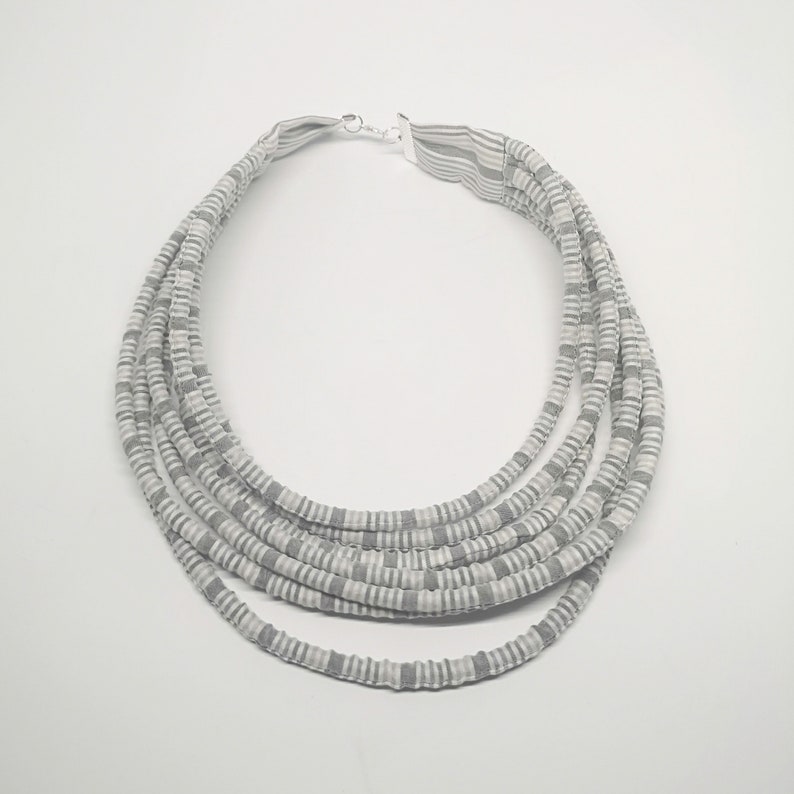 May include: A multi-strand necklace made of gray and white striped fabric. The necklace is layered and has a simple silver clasp.