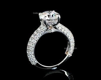 Può includere: Un anello di fidanzamento in argento con un grande diamante centrale trasparente a taglio rotondo. La fascia è incastonata con diamanti più piccoli, creando un effetto scintillante. L'anello è ambientato su uno sfondo nero.