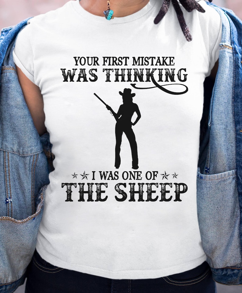 K&ouml;nnte beinhalten: Wei&szlig;es T-Shirt mit dem Text "YOUR FIRST MISTAKE WAS THINKING" &uuml;ber einer Silhouette einer Person, die ein Gewehr h&auml;lt. Darunter steht "I WAS ONE OF THE SHEEP".