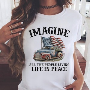 K&ouml;nnte beinhalten: Wei&szlig;es T-Shirt mit patriotischem Design. Die Grafik zeigt einen blauen und roten Oldtimer-Truck mit Blumen und einer amerikanischen Flagge. Der Text lautet "IMAGINE ALL THE PEOPLE LIVING LIFE IN PEACE."