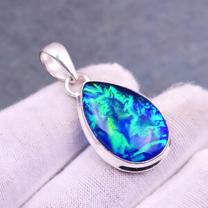May include: A teardrop-shaped pendant with a vibrant, iridescent opal stone. The opal displays shades of blue and green, set in a polished silver bezel. The pendant has a silver bail for a necklace chain.