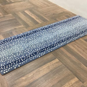 May include: A long rectangular runner rug featuring a gradient of blue tones ranging from light to dark. The surface is decorated with a repeating pattern of small, irregular white spots arranged in horizontal bands across the entire length.