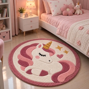 May include: A round area rug featuring a white unicorn with a gold horn, pink mane, and pink tail. The design includes two yellow stars and a pink heart on a cream background, surrounded by a wide, textured border in shades of pink and white.